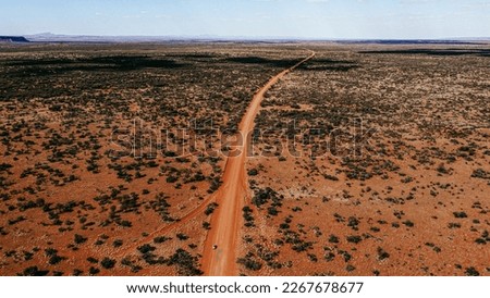 Car driving on a straight gravel road in the Australian red centre. Long orange road with trees on the side. Drone view of outback australia.  Royalty-Free Stock Photo #2267678677