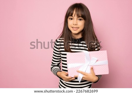 Picture of happy little girl child standing isolated over pink background. Looking camera holding gift box surprise.