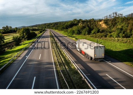 Truck with semi-trailer driving along highway on the sunset background. Goods delivery by roads. Services and Transport logistics. Modern Lorry Transport concept. Long Self-driving lorries Royalty-Free Stock Photo #2267691203