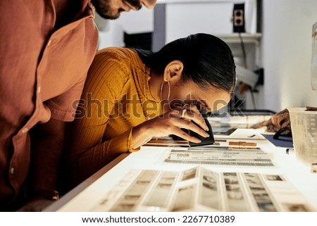 Photography, editing and film negatives for looking, magnifying glass or zoom analysis at photo journalist job. Photographer man, analyse or focus with woman in studio for creative choice in teamwork
