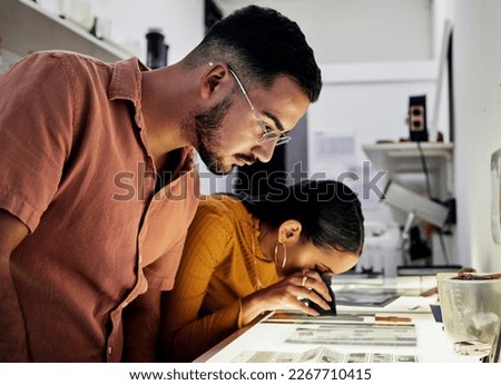 Photographer, editing and film negatives with looking, magnifying glass for zoom analysis at photo journalist job. Photography man, analyse or focus with woman in studio for creative decision in team