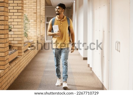 University student, college and indian man walking with a smile and backpack down campus corridor. Gen z male happy about education, learning and future after studying with scholarship at school Royalty-Free Stock Photo #2267710729