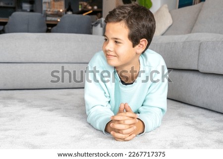 Happy childhood. Close up portrait of cheerful little boy smiling looking side, lying on floor at home.