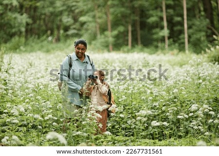 Portrait of black mother and daughter hiking in nature and looking in binoculars, copy space  Royalty-Free Stock Photo #2267731561
