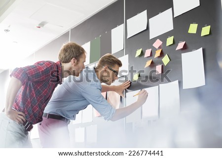 Businessmen analyzing documents on wall in office Royalty-Free Stock Photo #226774441