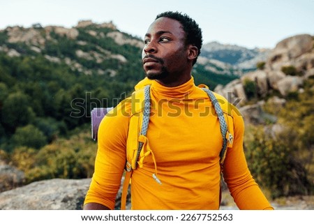 Hiker young adult african american man with backpack and trekking sticks at the foot of the mountain Royalty-Free Stock Photo #2267752563