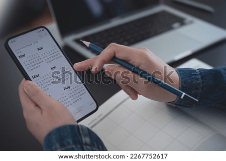 2023 Calendar event planner timetable agenda plan on organize schedule. Business woman using mobile phone with monthly calendar for event planning, Plan scheduling with laptop on office table
