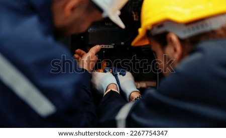 Close-up of two Caucasian production engineers in safety wear assisting in adjusting and maintaining CNC machine in the factory. Male factory workers are examining the industrial machine to fix it.