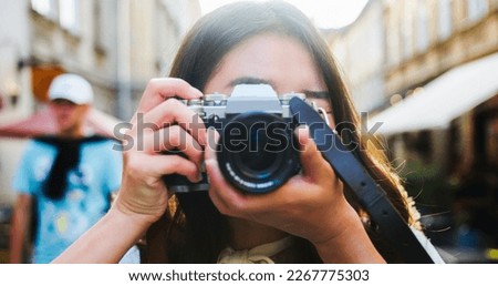 Close up portrait of cheerful beautiful female in good mood with camera standing outdoors in city. Happy pretty young Asian woman tourist taking photo. Photographer taking pictures. Urban concept