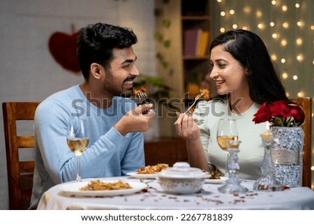 Happy young couple enjoying dinner by talking eachother during candle light dinner at home - concept of romantic moment, dating and togetherness Royalty-Free Stock Photo #2267781839