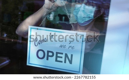 Woman wearing medical face mask hanging come in we're open sign on window; light effect