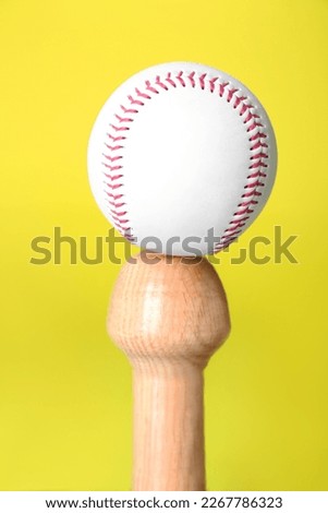 White ball on wooden baseball bat against yellow background, closeup. Sports equipment