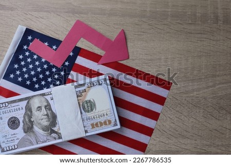 Red arrow going down on a background of money and US flag. The concept of changing course of US dollar on the market. Devaluation, collapse, stagnation of the economy. Royalty-Free Stock Photo #2267786535