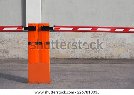 a closed red road barrier on an asphalt pre-house parking lot against the background of a gray building on a summer evening. pre-house car parking. limited parking.