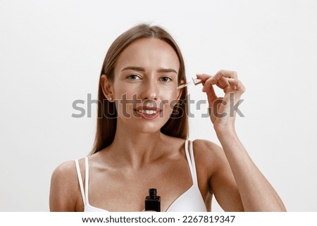 Woman applies on her face cosmetics moisturizing serum or oil, facial essence on studio background