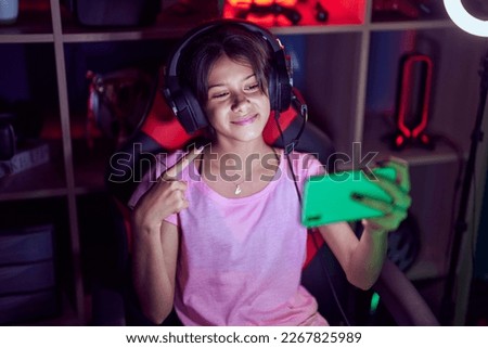Young girl playing video games with smartphone smiling happy pointing with hand and finger 
