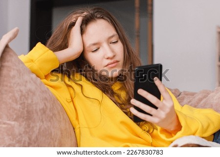 Upset young woman sit on couch at home hold smartphone receive unpleasant breakup text message, sad teen girl on sofa feel down read bad news on cellphone online, think of problem solution