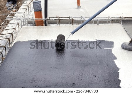 Worker applying a bituminous primer on a concrete slab at a construction site before laying bituminous waterproofing Royalty-Free Stock Photo #2267848933