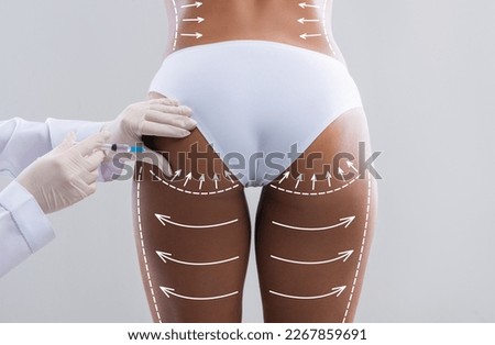 Young slim black woman in white bikini with abstract lines gets injection from beautician in hips isolated on gray wall background, studio, back. Beauty care, body shaping, medical care and buttocks Royalty-Free Stock Photo #2267859691