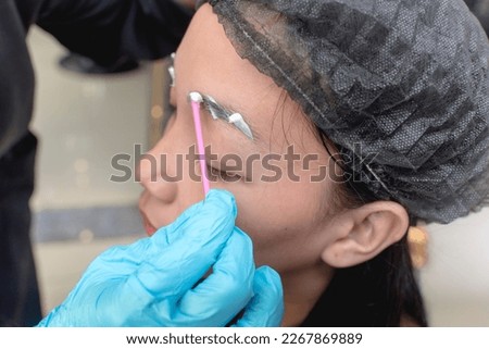 An esthetician applies numbing cream or topical anesthesia to a clients eyebrows prior to a microblading procedure.