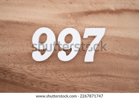 White number 997 on a brown and light brown wooden background.