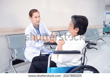 Smiling female doctor caring for elderly woman patient in wheelchair. At hospital. Medical concept.