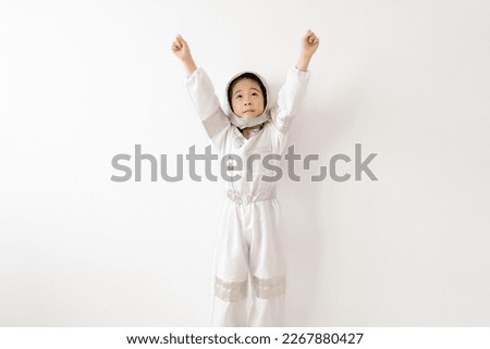 Portrait of cute little Asian girl in space suit playing astronaut and with arms up , looking up on white wall background. Childhood, creative and imagination. Asia kid child girl funny moments.