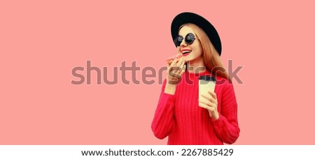 Portrait of modern young woman eating donut drinking coffee isolated on pink background