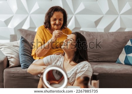 Smiling grandmother applying makeup on her granddaughter. Candid moment of affection between grandmother and adult granddaughter. Royalty-Free Stock Photo #2267885735
