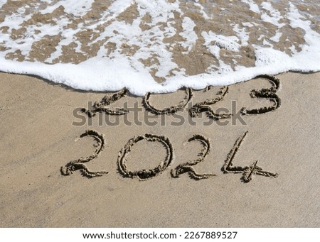 New Year 2024 is coming concept - inscription 2023 and 2024 on a beach sand, the wave is starting to cover the digits 2023 Royalty-Free Stock Photo #2267889527