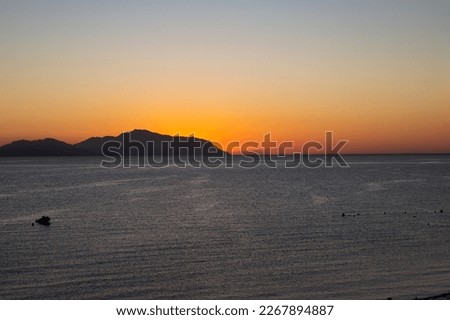 Horizon view from the sea, beautiful bright orange yellow sunset in the mountains, calm dark blue ocean water