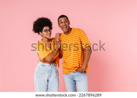 Positive smiling african couple in casual wear looking away at copy space isolated over pink studio background Royalty-Free Stock Photo #2267896289