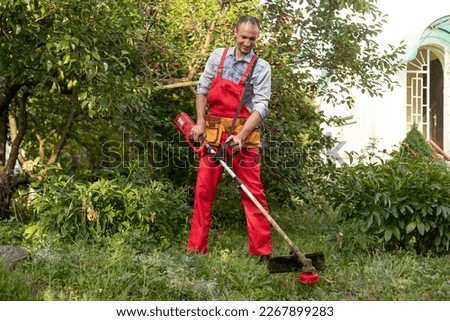Mowing grass with electric lawn mower. Garden work concept. Man mows the grass with hand mower in the garden Royalty-Free Stock Photo #2267899283