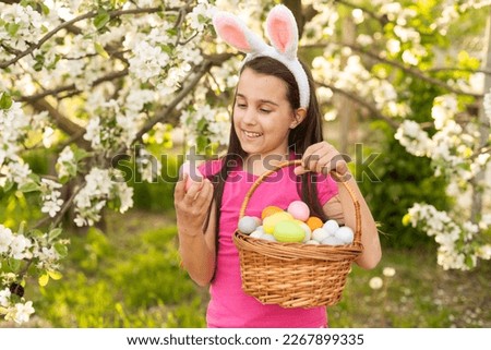 A little girl with pink rabbit ears. painted eggs in the park. Easter. Copy space.