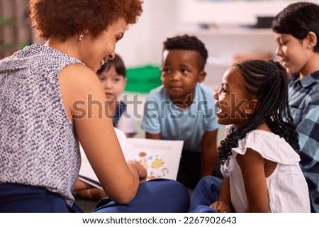 Female Teacher Reads To Multi-Cultural Elementary School Pupils Sitting On Floor In Class At School Royalty-Free Stock Photo #2267902643