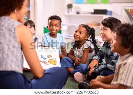 Female Teacher Reads To Multi-Cultural Elementary School Pupils Sitting On Floor In Class At School Royalty-Free Stock Photo #2267902663