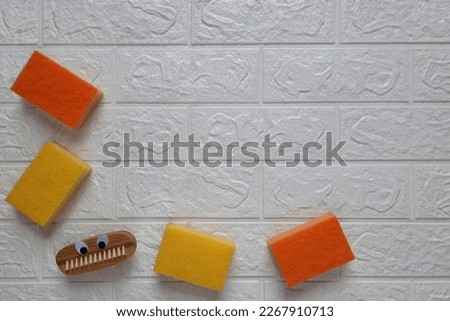 Fun brush and kitchen sponges for cleaning. Copy space. Fun cleaning concept.  Scrubbing brush with eyes and dishwashing sponge on brick wall background. Flat lay. Household duties for children.