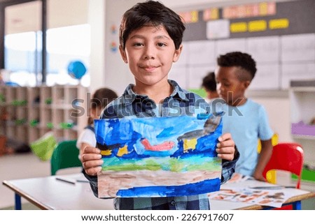 Classroom Portrait Of Proud Male Elementary School Pupil Holding Painting In Art Class At School