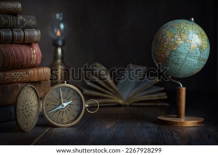 Old earth globe, compass, books and lamp on the table. In the cabinet of a traveler, explorer, investigator, discoverer. Concept on the theme of travel, world exploration,  antiquity, history.  Royalty-Free Stock Photo #2267928299