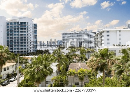 Taken from a balcony of a building in the West Avenue neighborhood in Miami Beach, towers and shops around, tropical plants, parked cars on the street and urban and tropical landscape