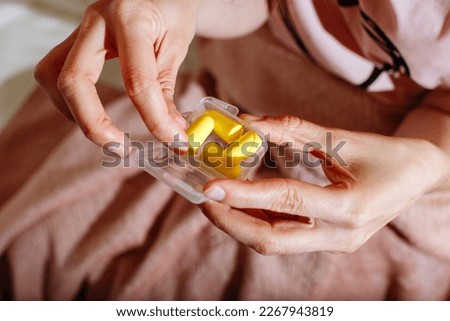Close up of female hands and yellow earplugs. Woman holding a box of earplugs. Light background. Copy space Royalty-Free Stock Photo #2267943819