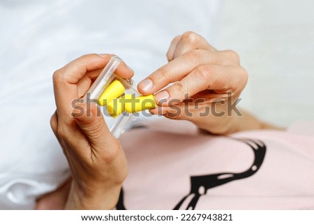 Close up of female hands and yellow foam earplugs. Woman taking the antinoise earplug. Light background. Free space for text. Royalty-Free Stock Photo #2267943821