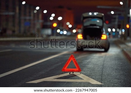Broken down car on city street at night, red triangle - emergency stop sign behind broken blurred car. Alone damaged car at night on city highway
