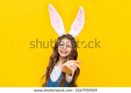A happy little girl is enjoying Easter. Spring holiday for children. A child dressed as a rabbit with long ears. A charming lady with curly hair on a yellow isolated background.