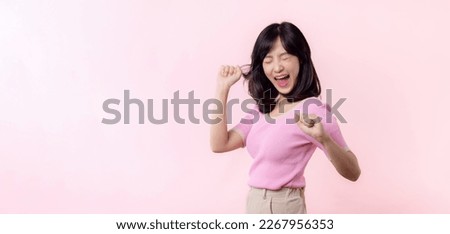 Portrait young beautiful asian woman happy smile dance with fist up victory gesture expression cheerful her success achievement against pink pastel studio background. Woman day celebration concept.