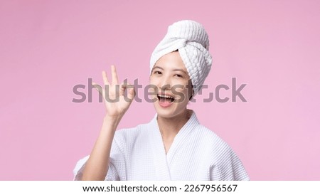Young beautiful asian woman happy smile face with hand or finger gesture signs in bathrobe and shower towel showing empty space isolated on pink background.