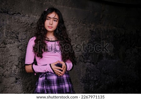 Teenage girl dressed in gothic style posing standing with concrete wall in background