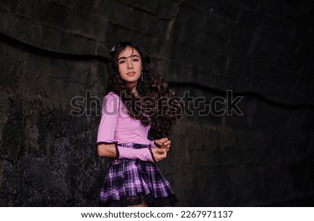 Teenage girl dressed in gothic style posing standing with concrete wall in background