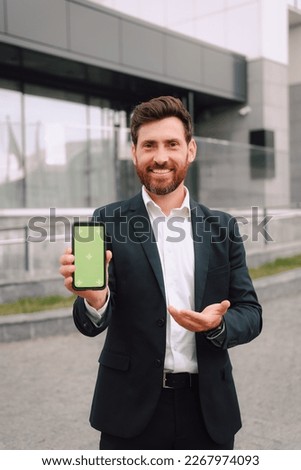 Smartphone With Blank Screen In Businessman Hand, Smiling Middle Eastern Male Entrepreneur Showing For Mobile App Or Website Advertisement While Posing Outdoors, Mockup Royalty-Free Stock Photo #2267974093