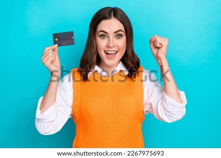 Photo of overjoyed positive woman bob hairstyle orange waistcoat staring holding card raising fist isolated on teal color background